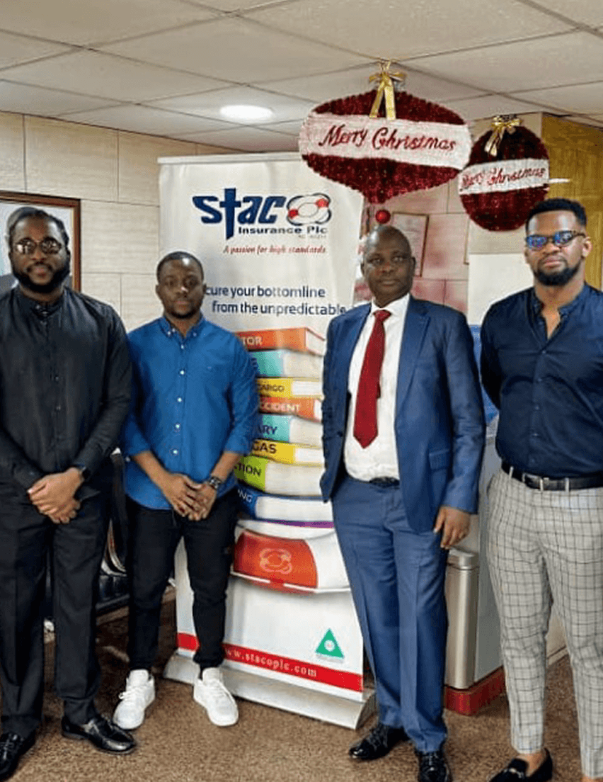 A group photo at a Staco Insurance office beside a Staco Insurance banner, decorated for the holidays